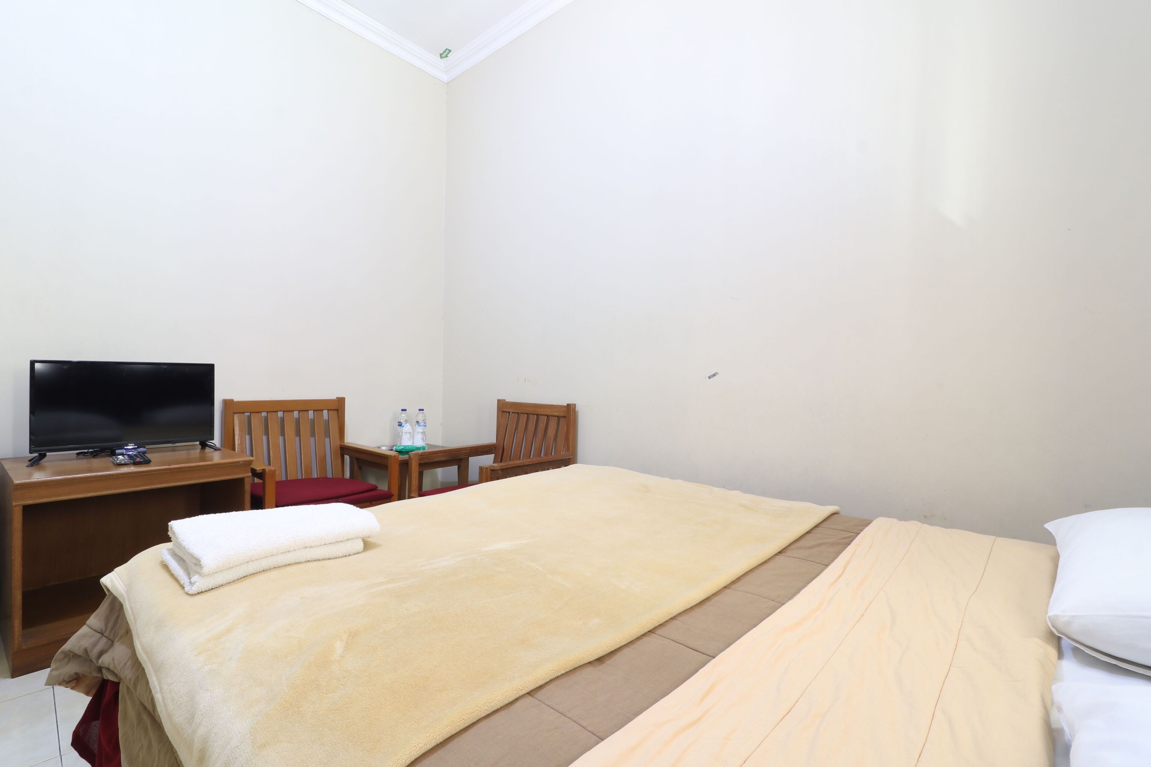 A hotel room with a bed, a TV, a wooden chair, a small table with bottles, and a red towel.