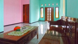 A spacious room with a wooden bench, a table with a placemat, and a door leading to another room. - Kawah Ijen Homestay (Banyuwangi)