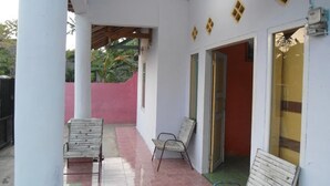 A covered outdoor area with two chairs, a red wall, and a door leading inside. - Kawah Ijen Homestay (Banyuwangi)
