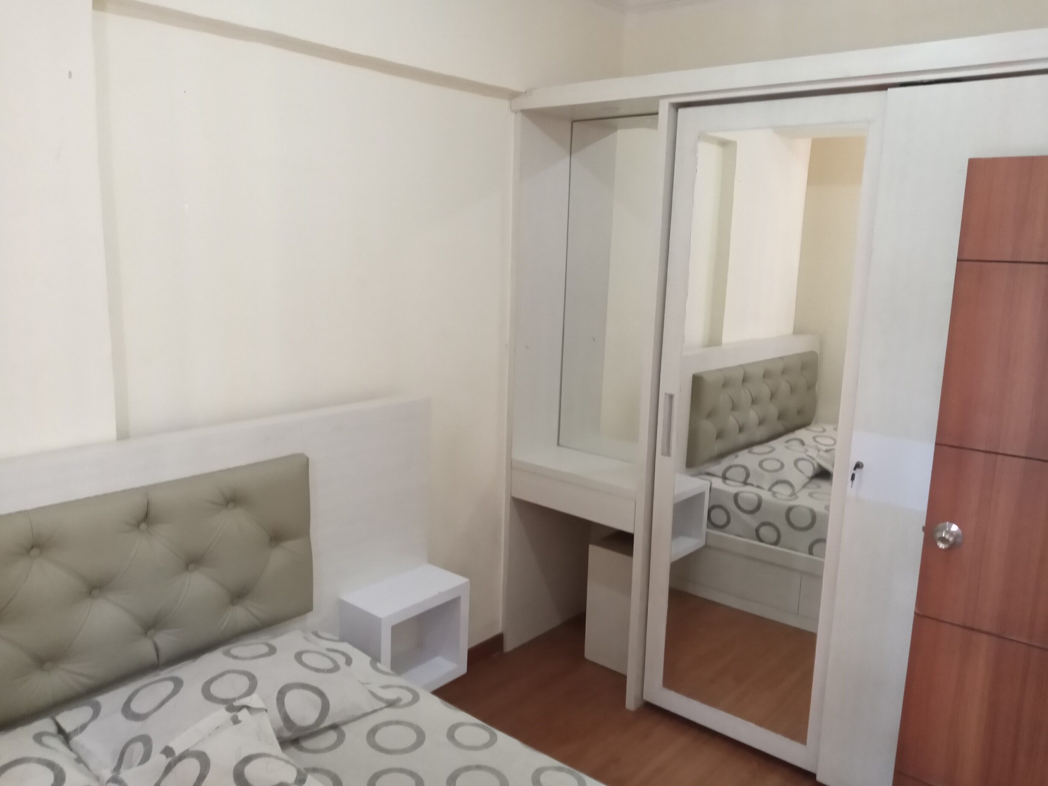 A bedroom with a bed, a wardrobe, a mirror, and a small bedside table.