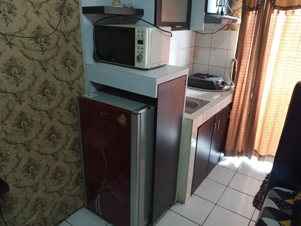 Una cocina compacta con microondas, refrigerador y un lavamanos pequeño.