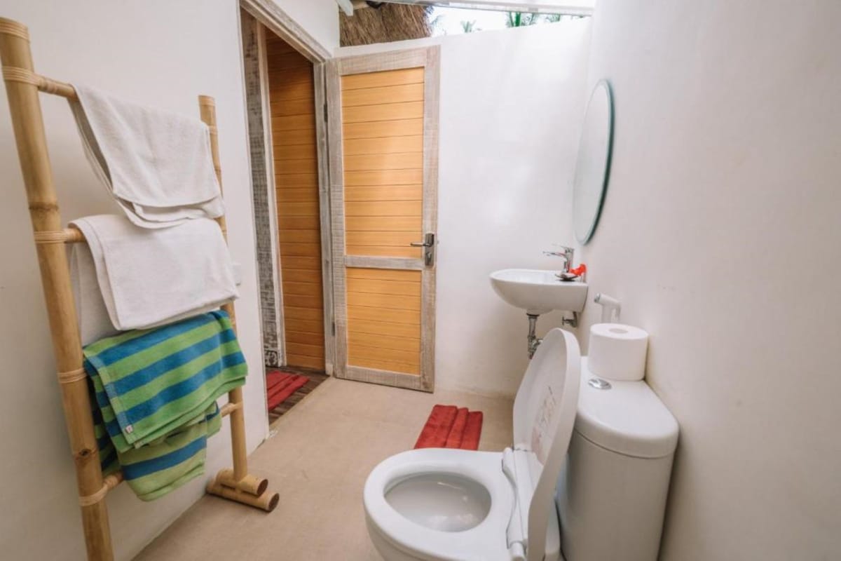 Une petite salle de bain compacte, équipée de toilettes, d’un lavabo et d’une porte en bois donnant sur une autre pièce.