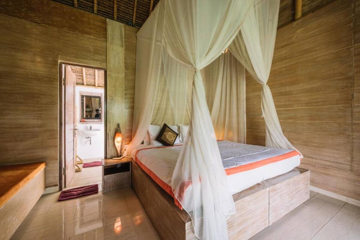 Een slaapkamer met een hemelbed, houten vloeren, een nachtkastje en een bedtafel.