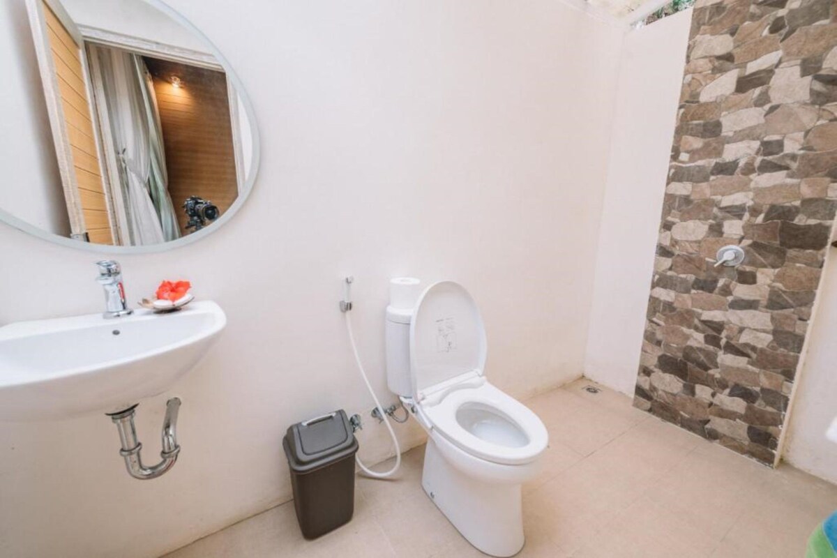 Une salle de bain avec un lavabo blanc, des toilettes et une douche avec un mur en pierre.