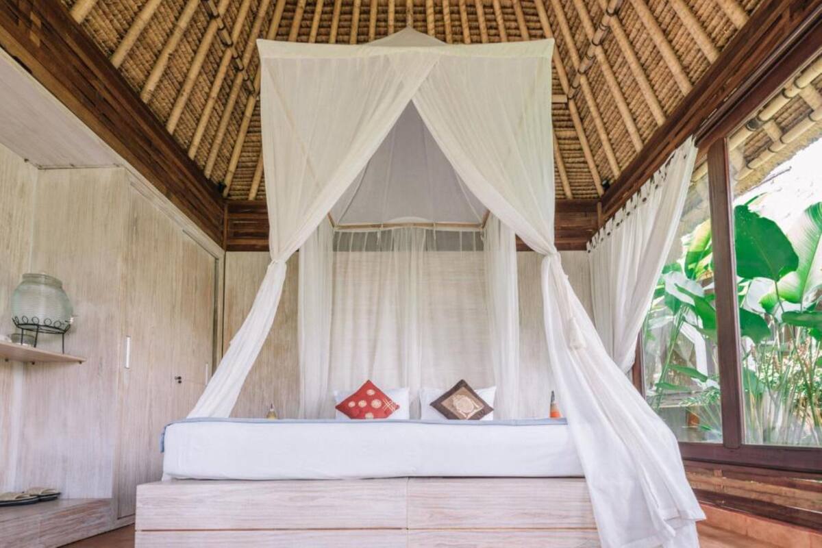 Een kamer met een bed onder een baldakijn, houten wanden en een raam met planten.