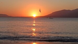 Um pôr do sol sobre um mar calmo, com barcos e montanhas ao fundo.