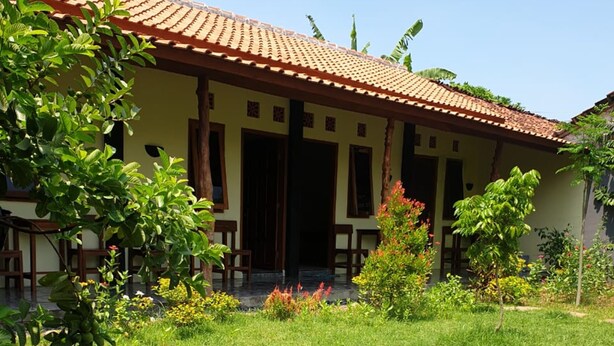 Uma casa com telhado ladrilhado e um jardim com diversas plantas e um caminho.
