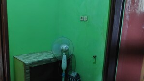 A room with a green wall, a small wooden table, a trash bin, and a standing fan. - Homestay Ngudi (Mangunan)