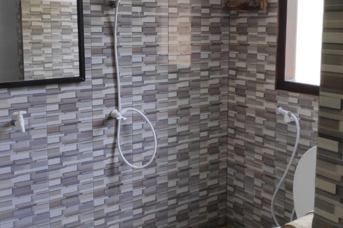 Un baño con pared de azulejos, inodoro, ducha y ventana.