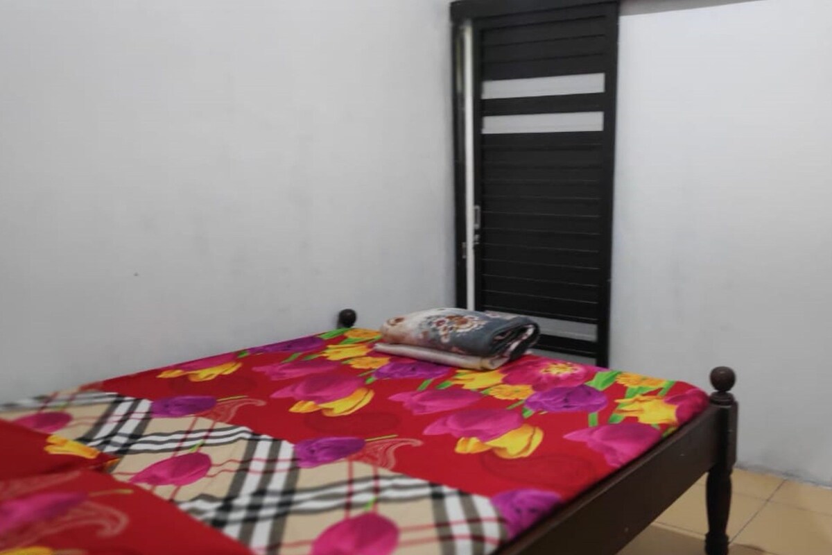 A small, simple room with a bed, a window with a black shutter, and a tiled floor.