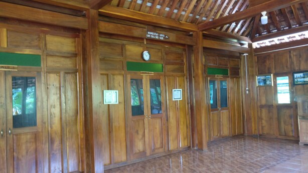 A wooden interior with a clock, signs indicating 'HOMESTAY: JOYO' and 'HOMESTAY: MAWAR'. - Homestay Arya Mangunan (Mangunan)