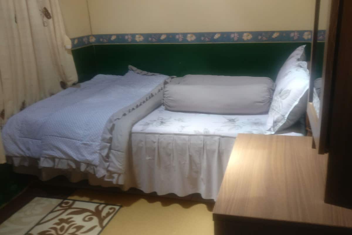 A single bed with a green headboard, white bedding, and a patterned curtain.
