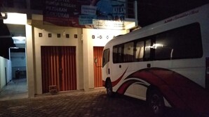 A bus parked outside a building with a closed red gate and a signboard above the entrance. - Rumah Singgah Peziarah Ganjuran (Sumbermulyo)