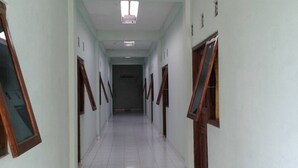 A long, narrow hallway with white tiled floors and wooden doors on both sides. - Rumah Singgah Peziarah Ganjuran (Sumbermulyo)