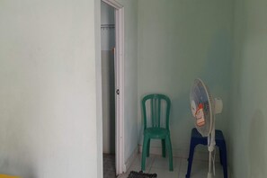 A room with a door leading to a bathroom, a green plastic chair, and a standing fan. - Rumah Singgah Peziarah Ganjuran (Sumbermulyo)