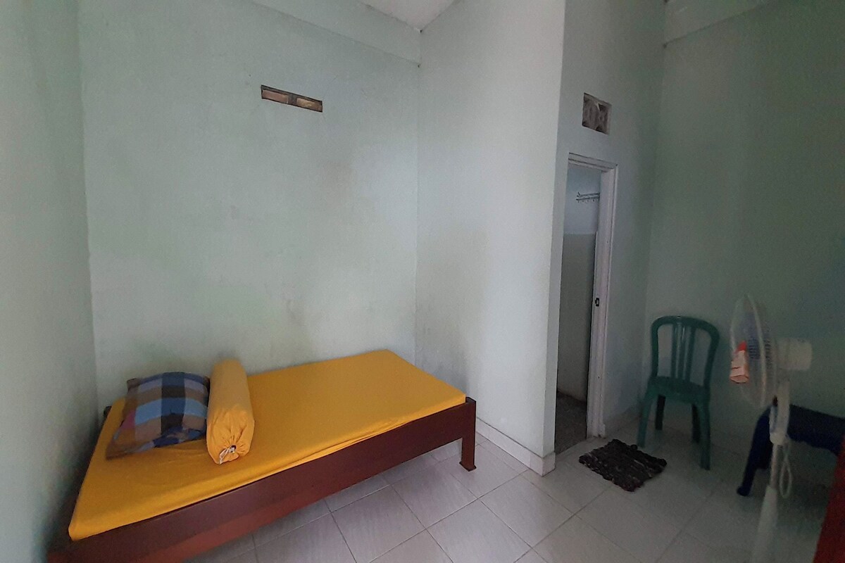 Une petite pièce simple, avec un lit, une porte et une chaise.