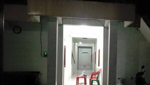 A narrow hallway leading to a room with a bed, a nightstand, and a chair. - Rumah Singgah Peziarah Ganjuran (Sumbermulyo)