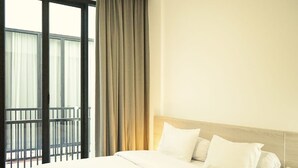 A hotel room with a large bed, a wooden headboard, a nightstand, and a view of a balcony with curtains.