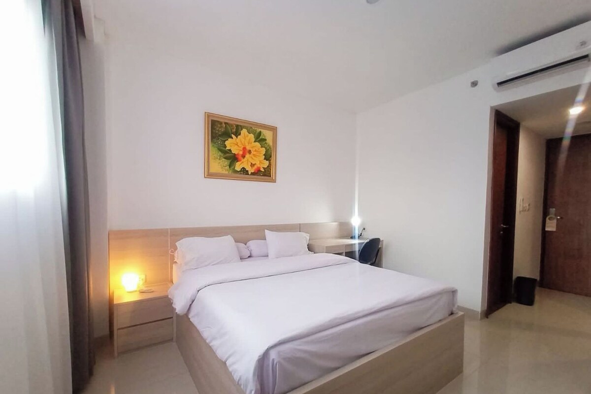 Quarto de hotel com uma cama grande, mesas de cabeceira, uma escrivaninha e um ar condicionado fixado na parede.