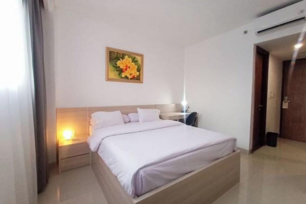 A hotel room with a bed, bedside table, lamp, and a painting on the wall.