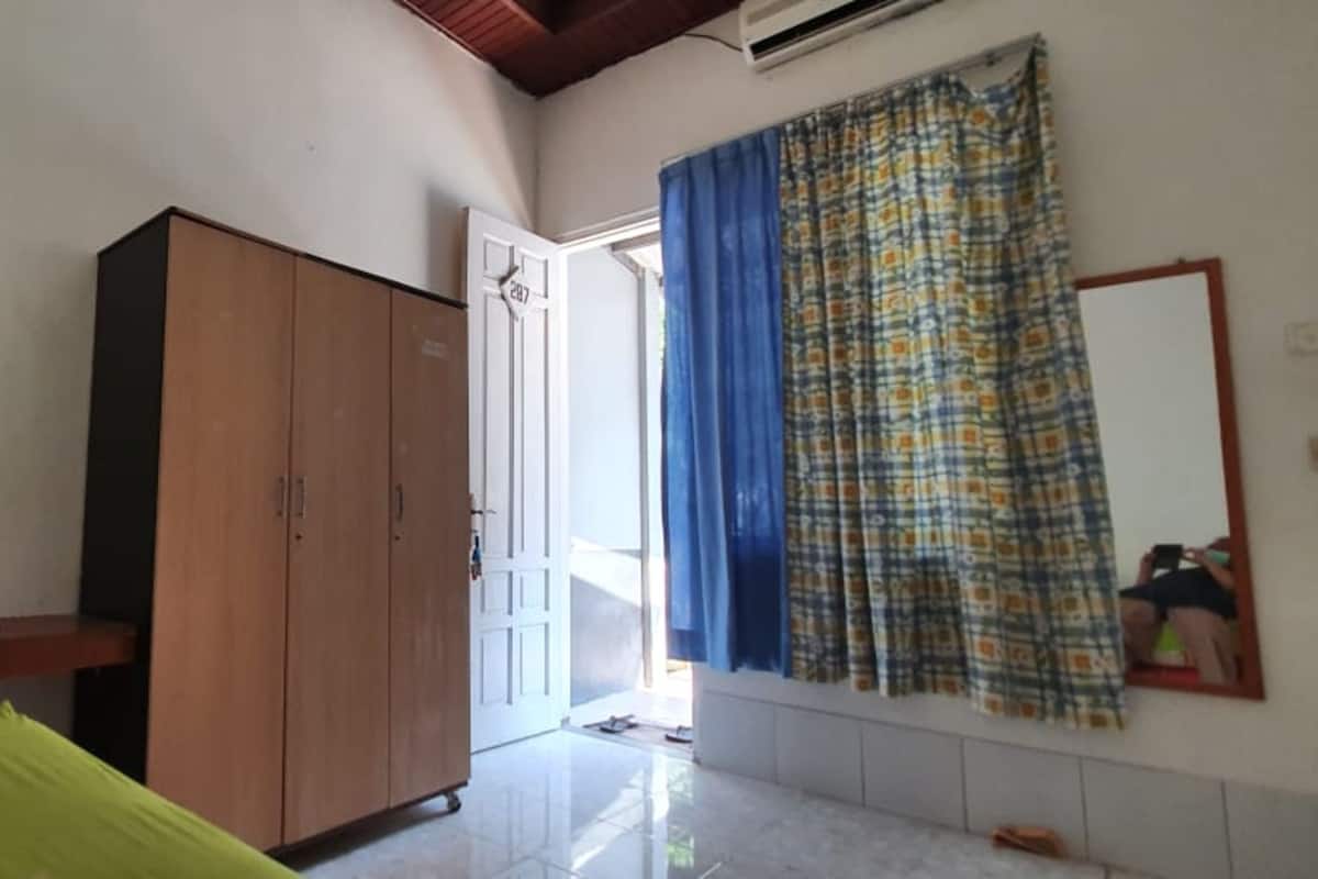 Quarto com cama, guarda-roupa, televisão na parede e janela com cortinas.