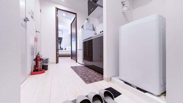 A hallway with a white refrigerator, a microwave, and a red fire extinguisher. There are slippers on a rug and a door leading to another room. - Sunshine Tower 202 (Tokyo)