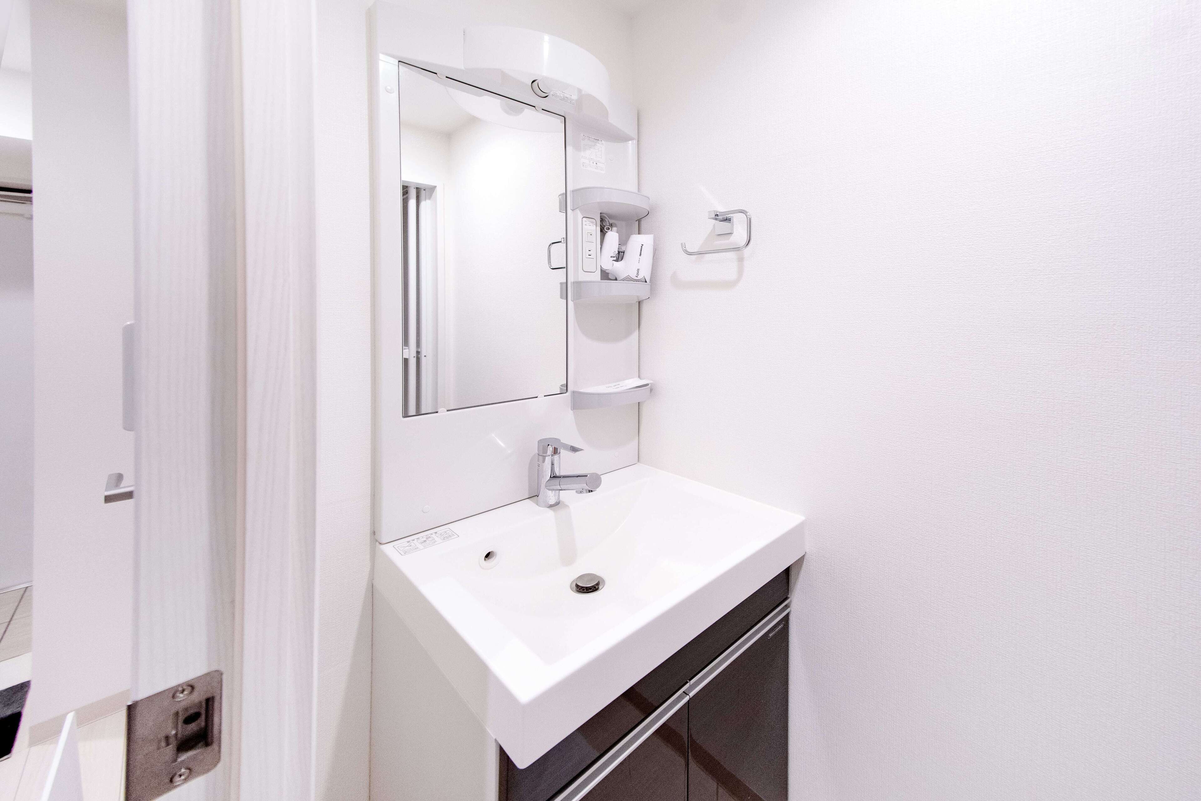 Un baño con lavamanos blanco, espejo y perchero.