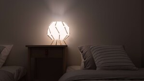 A dimly lit room with a hexagonal light fixture on a bedside table, a bed with striped pillows, and a nightstand with a drawer. - Starry Night Dreams of Stars House (Tokyo)