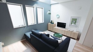 A modern living room with a dark blue sofa, a flat-screen TV, a small wooden cabinet, and a green side table. - Starry Night Dreams of Stars House (Tokyo)