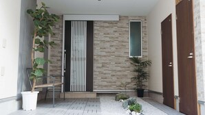 A modern entrance with a stone wall, a bench, a potted plant, and a door. - Starry Night Dreams of Stars House (Tokyo)