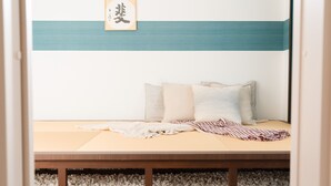 A minimalist room with a low bed, a framed calligraphy piece, and a teal stripe on the wall. - Back to 90s American Style House (Tokyo)