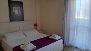 Ein Hotelzimmer mit Bett, Nachttisch, roter Lampe, Klimaanlage und einem fenster mit Vorhängen.