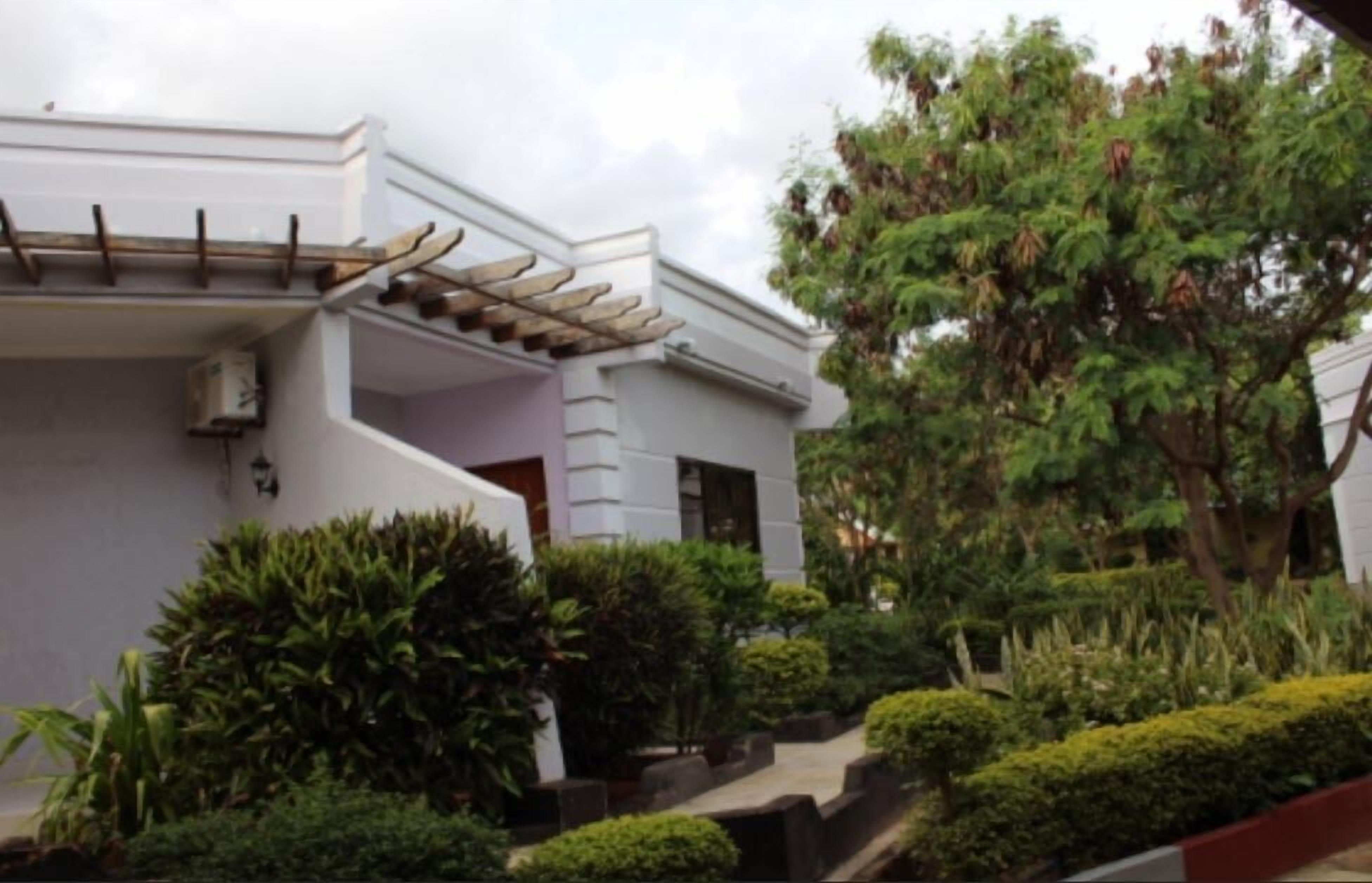 A modern building with a white facade, a covered porch, and a well-maintained garden with various shrubs and a large tree.