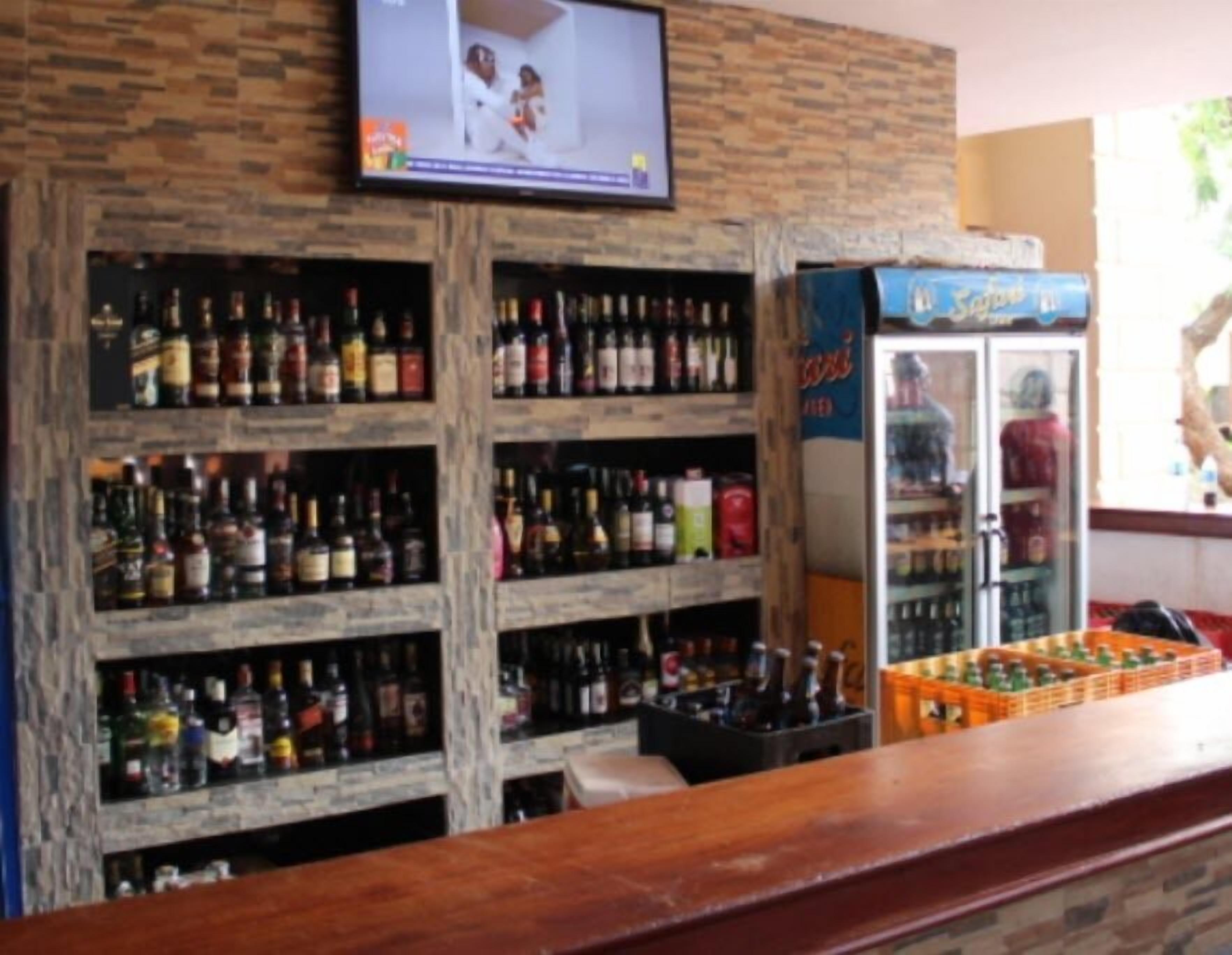 A bar area with shelves of liquor bottles, a television mounted on the wall, and a refrigerator with beverages.