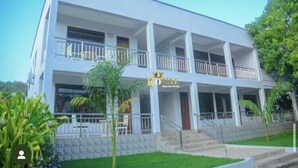 A two-story hotel with a white facade, balconies on each floor, and a stone base. - Royal Village Hotel Company (Dodoma)