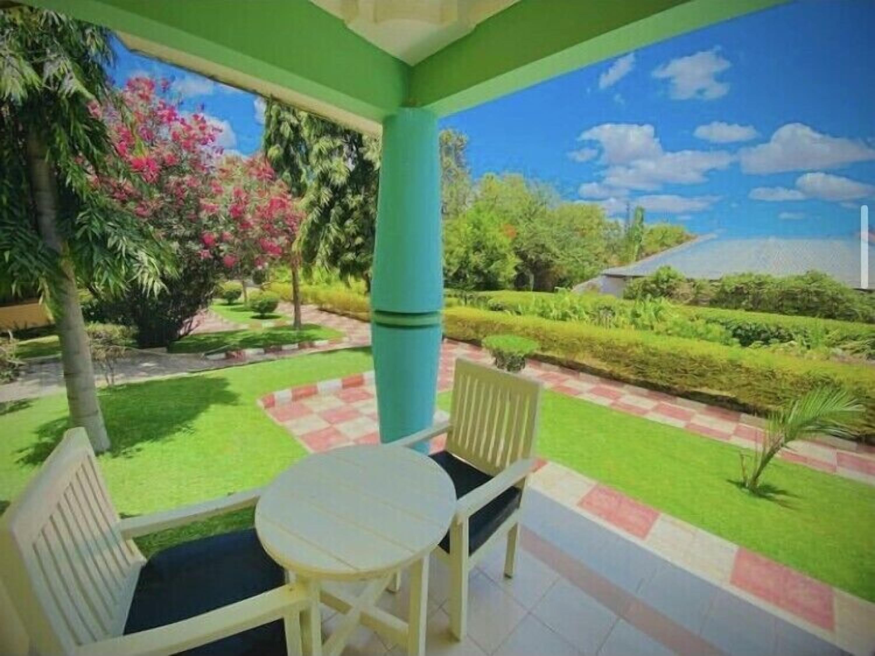 A covered outdoor seating area with a view of a garden and a clear sky.