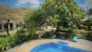 A swimming pool surrounded by lush greenery and a tree. - Royal Village Hotel Company (Dodoma)