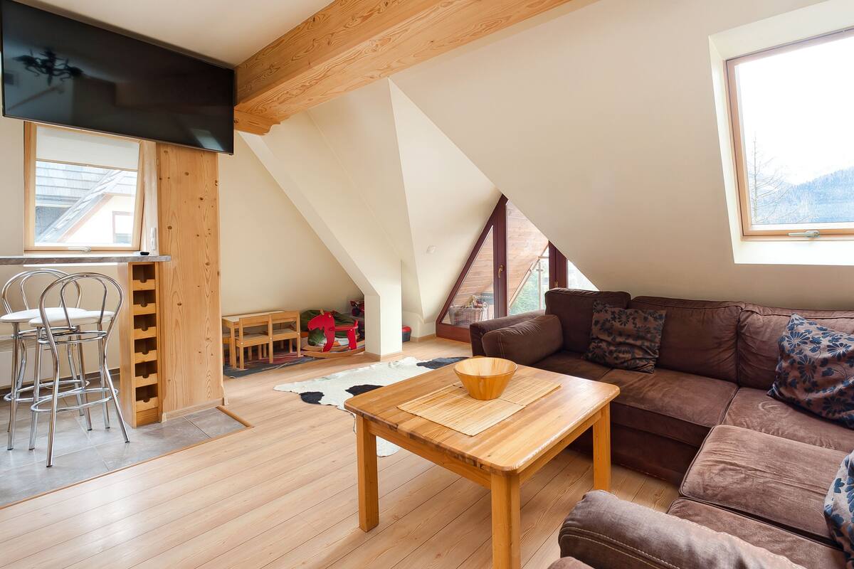 Un salon chaleureux, aménagé dans un style industriel, avec une table en bois, un canapé marron et une grande fenêtre donnant sur l’extérieur.