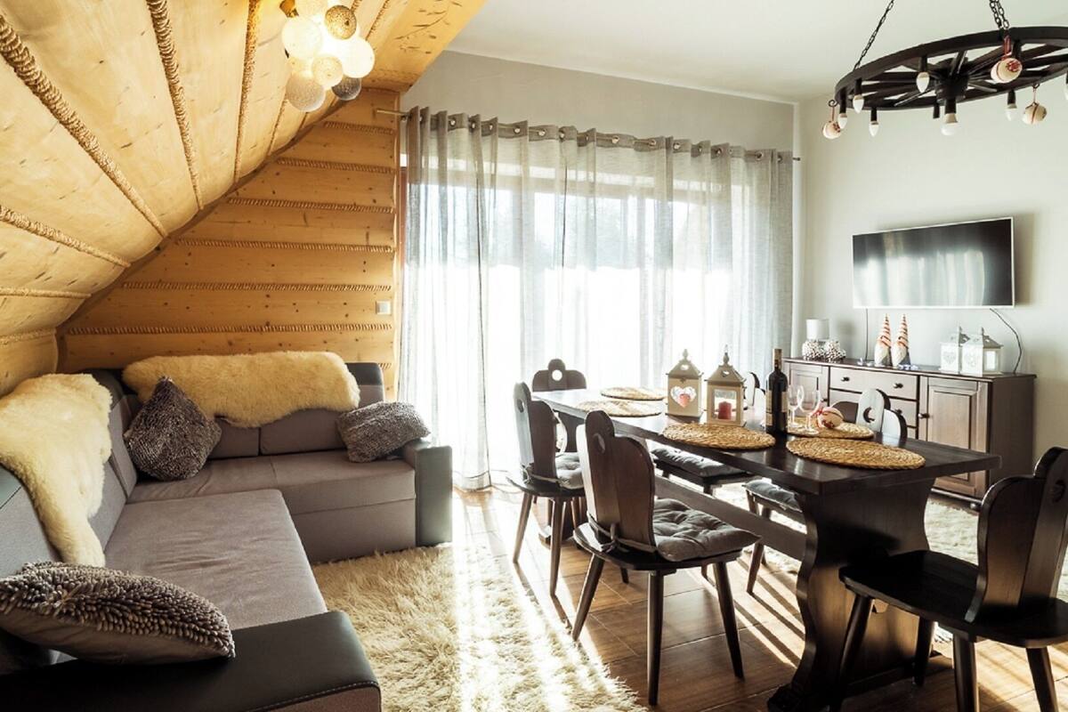 Une pièce chaleureuse, aménagée dans le style d’un chalet en bois, avec un canapé, une table à manger, des chaises et un lustre.
