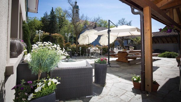 An outdoor patio area with wicker furniture, potted plants, and a large umbrella providing shade. - Hotel Bären (Rupperswil)