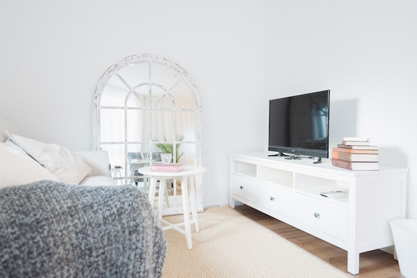 A modern living room with a white sofa, a white TV stand, and a small table with a plant.