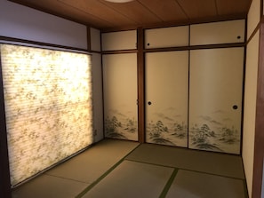 A traditional Japanese room with tatami flooring, shoji screens, and sliding doors with landscape paintings.