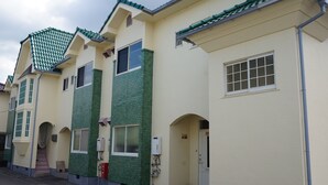 A row of residential buildings with green-tiled roofs and beige walls, featuring multiple windows and a visible staircase.