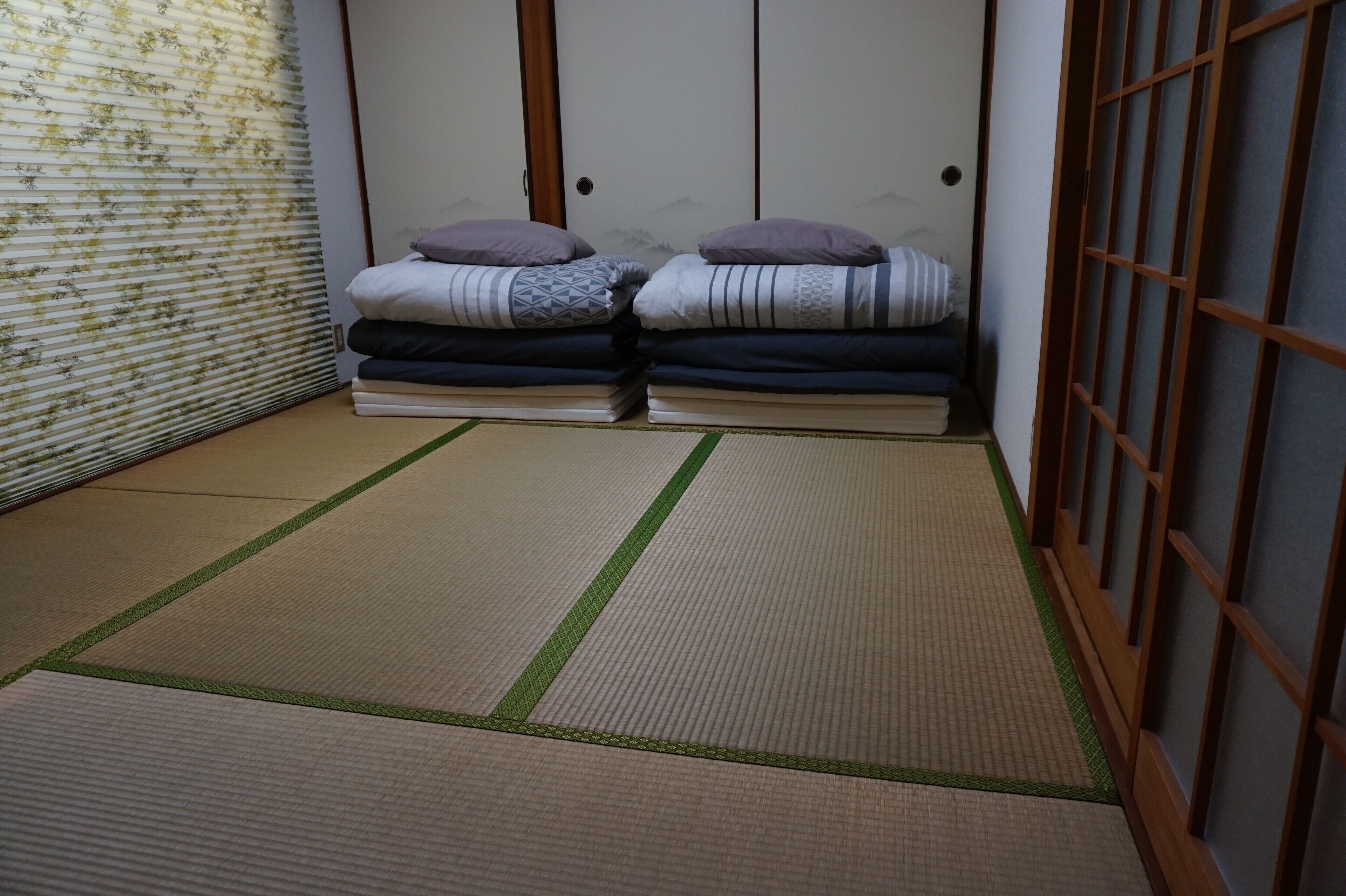 A tatami mat room with a shoji screen, two beds with pillows, and a sliding door.