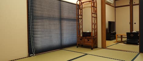 Una habitación con esteras de tatami, una puerta corredera, un estante de madera y un televisor.