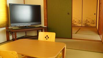 A traditional Japanese room with tatami flooring, a low table, a television on a stand, and sliding doors.