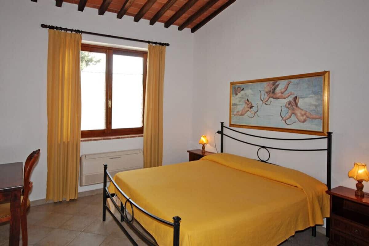 A bedroom with a bed, a desk, a chair, a window with curtains, a painting on the wall, and two bedside lamps.