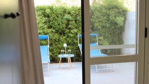 Un espacio al aire libre con sillas azules y una pequeña mesa, rodeado de abundante follaje verde.