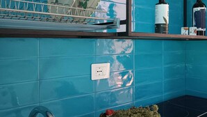 A kitchen with a blue tiled backsplash, a dish rack, a bottle of wine, a basket of greens, and a plate of bread. - Le Barchette 5 - piano terra (Lecce)