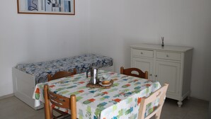 Una habitación pequeña y ordenada, con una cama, una mesa con mantel, una cafetera y un armario.